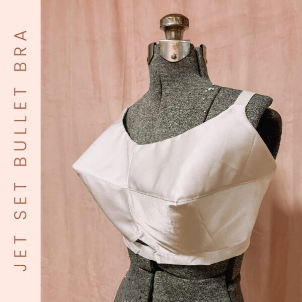Displayed against a pink backdrop, a mannequin showcases the Jet Set Natural Bra Pattern, a vintage-style bullet bra. It is pale and structured with pointed cups and wide straps, with "JET SET BULLET BRA" written vertically on the left.