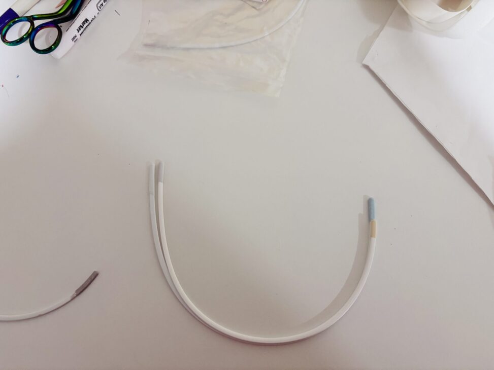 A curved white tube with colored ends lies on a white surface, surrounded by scissors, packaging, and other materials—tools often seen when working on a Madalynne Fiona Bra sewing project for a detailed pattern review.