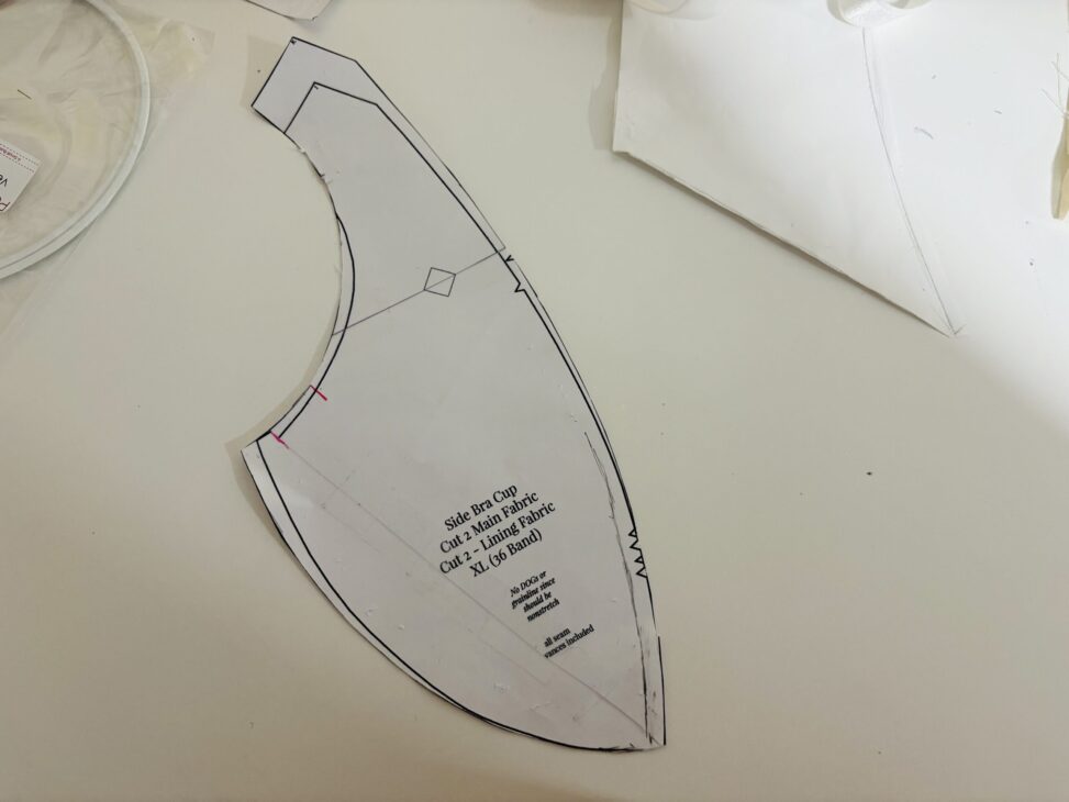 A paper sewing pattern piece for a bra cup, labeled "Side Bra Cup" with cutting instructions and guidelines, lies on a white surface with other Madalynne Fiona Bra pattern pieces—perfect for your next Pattern Review.